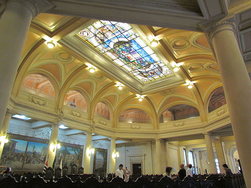 Interior da antiga sede da Bolsa do Café, com vitral colorido no teto, colunas neoclássicas e pinturas históricas nas paredes