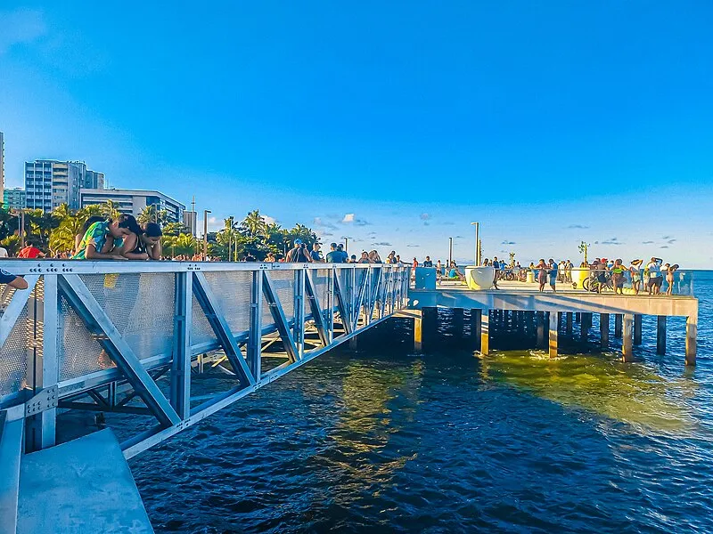Pessoas reunidas no Marco dos Corais em Maceió, sobre passarela metálica sobre o mar