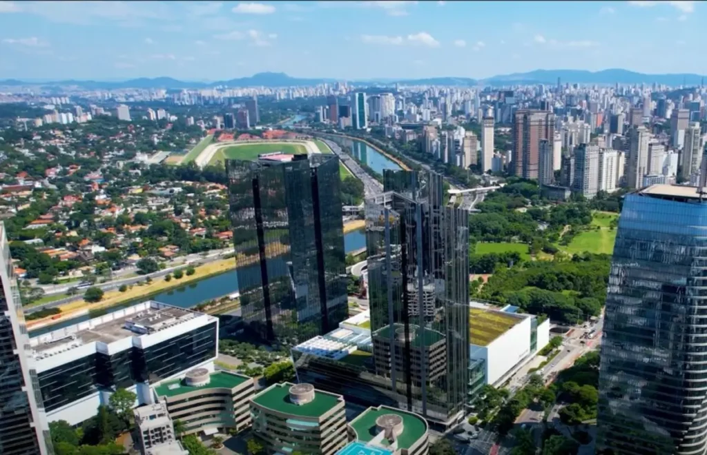 Vista aérea da Marginal Pinheiros em São Paulo, com prédios modernos, o rio Pinheiros e o Jockey Club ao fundo