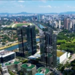 Vista aérea da Marginal Pinheiros em São Paulo, com prédios modernos, o rio Pinheiros e o Jockey Club ao fundo