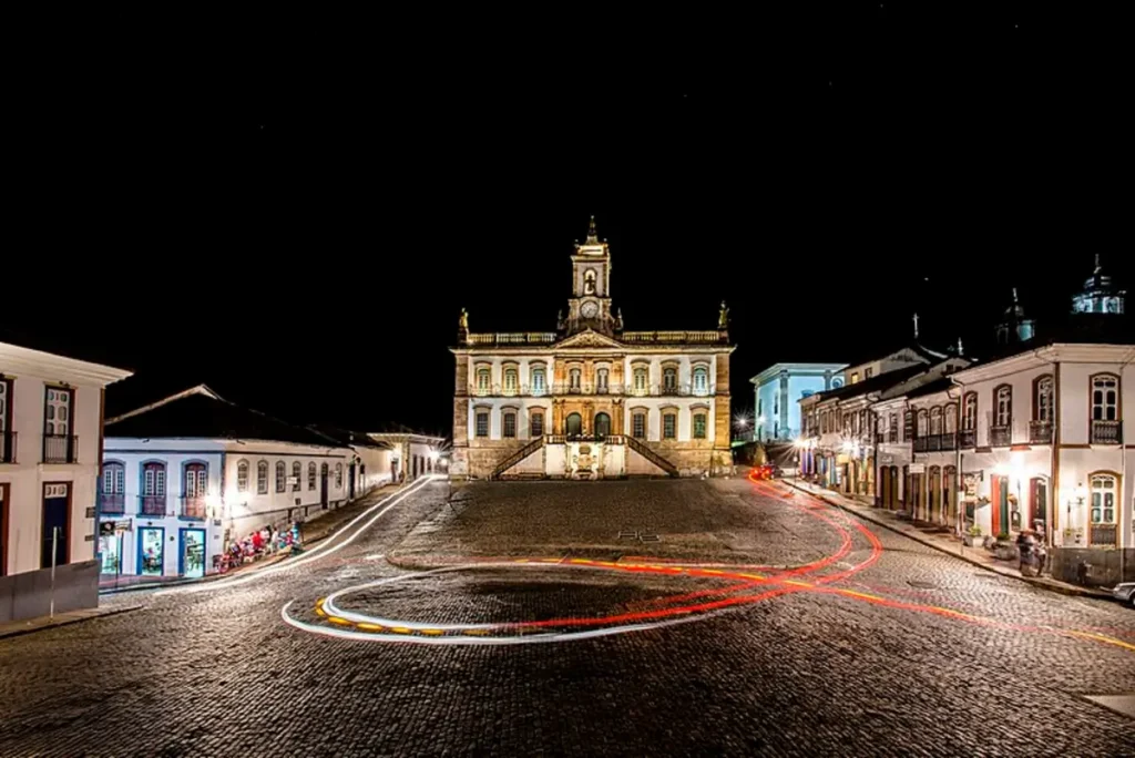 Fachada iluminada do Museu da Inconfidência à noite, em Ouro Preto, com trilhas de luz deixadas pelos veículos nas ruas de paralelepípedo