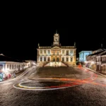 Fachada iluminada do Museu da Inconfidência à noite, em Ouro Preto, com trilhas de luz deixadas pelos veículos nas ruas de paralelepípedo
