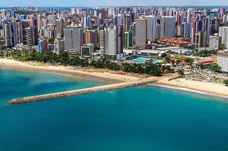 Vista aérea da praia de Fortaleza com mar azul e prédios modernos ao fundo
