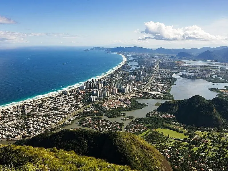 Vista aérea da Barra da Tijuca no Rio de Janeiro com edifícios, praia e áreas verdes ao fundo
