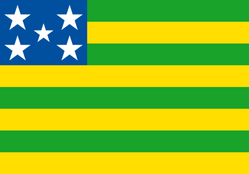 Bandeira do estado de Goiás com listras verdes e amarelas e estrelas brancas sobre fundo azul. Domínio público, via Wikimedia Commons