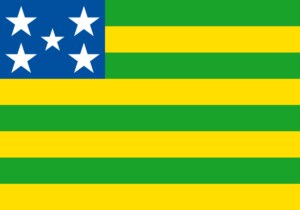 Bandeira do estado de Goiás com listras verdes e amarelas e estrelas brancas sobre fundo azul. Domínio público, via Wikimedia Commons