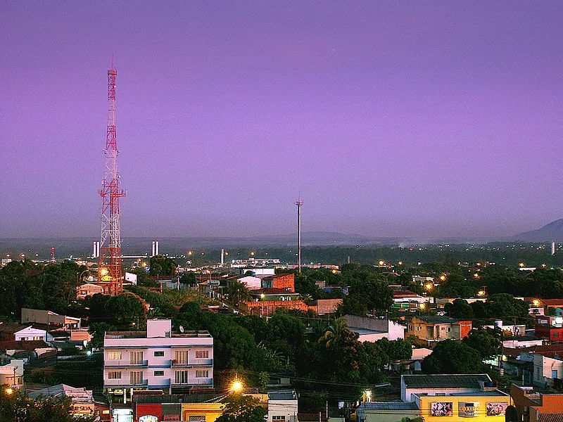 Vista noturna de Cuiabá com torres iluminadas e céu roxo