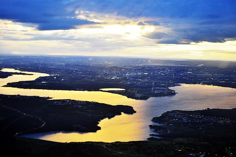 Vista aérea do Lago Paranoá ao pôr do sol, com reflexo dourado na água e Brasília ao fundo