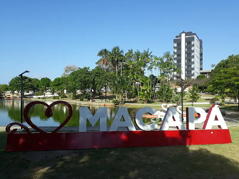 "Eu amo Macapá" em parque urbano com lago e prédios ao fundo