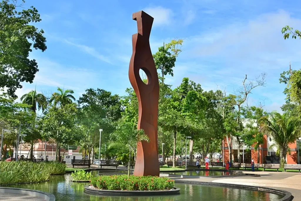 Escultura moderna na Praça da Revolução em meio a árvores e espelho d'água. Por MTur Destinos, Attribution, via Wikimedia Commons