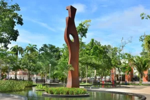 Escultura moderna na Praça da Revolução em meio a árvores e espelho d'água. Por MTur Destinos, Attribution, via Wikimedia Commons