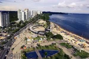 Vista aérea da Praia da Ponta Negra em Manaus com calçadão, prédios e o rio ao fundo