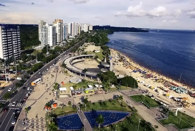 Vista aérea da Praia da Ponta Negra em Manaus com calçadão, prédios e o rio ao fundo