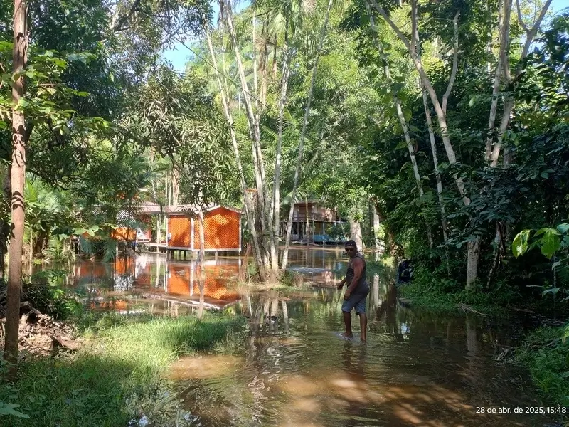 Casa ribeirinha nas margens do rio em Santana, Amapá, com homem caminhando em área alagada naturalmente