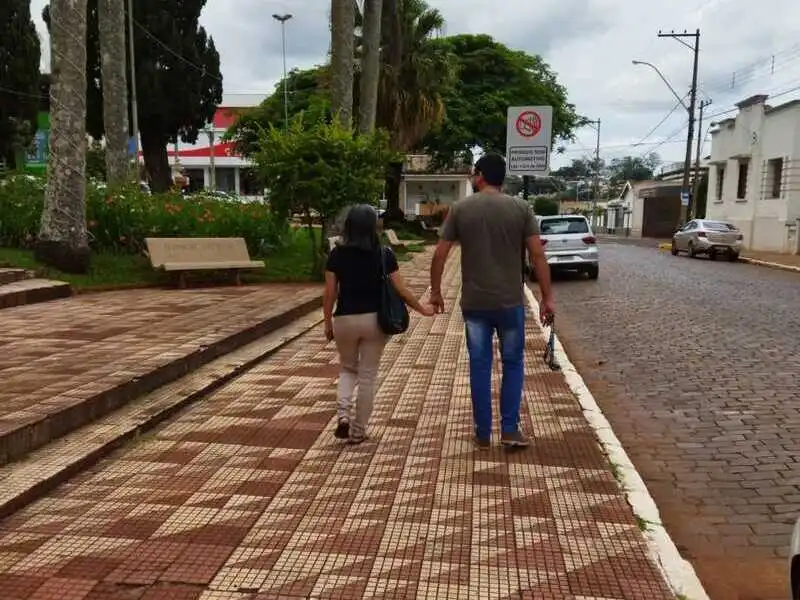 Casal caminhando de mãos dadas por uma calçada em cidade do interior