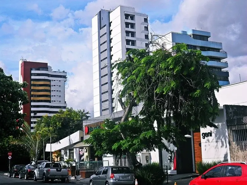 Prédios e comércios no bairro Kalilândia em Feira de Santana BA, mostrando área urbana moderna com veículos e árvores.