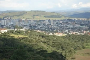 Vista panorâmica da cidade de Lages, Santa Catarina, com prédios ao fundo e morros cobertos de vegetação