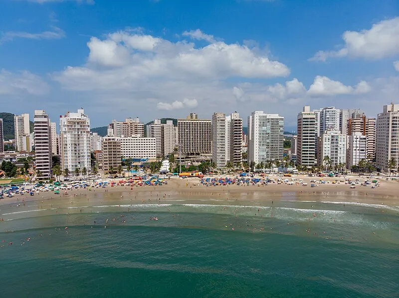 Vista aérea da Praia da Enseada no Guarujá com prédios à beira-mar e banhistas na faixa de areia