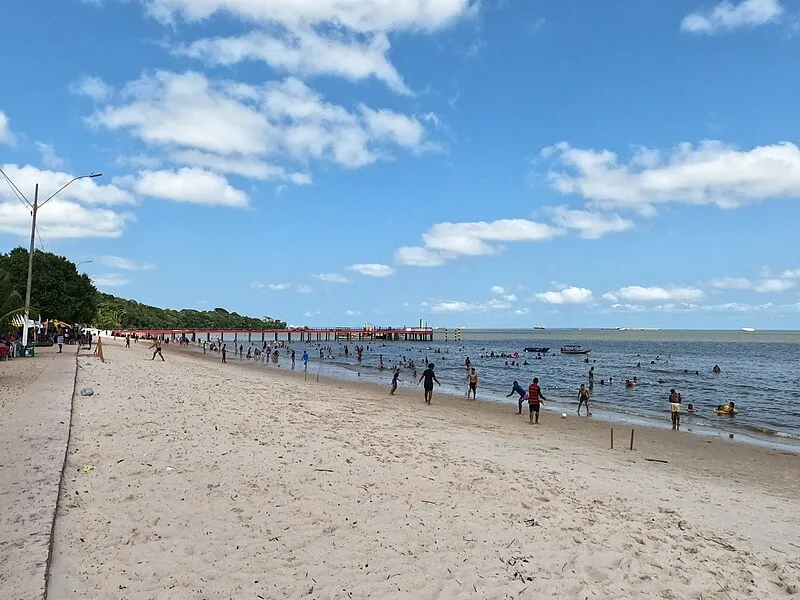 Praia do Caripi em Barcarena, Pará, com banhistas e trapiche ao fundo