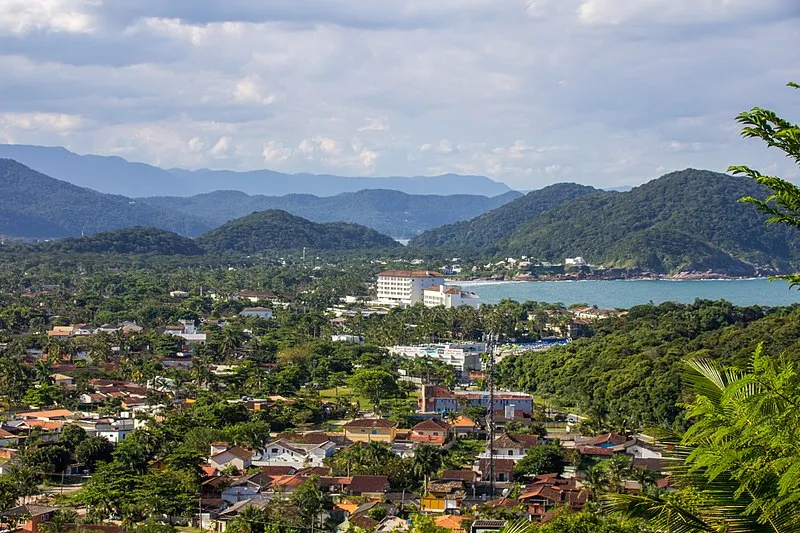 Vista panorâmica do Guarujá com vegetação tropical, morros ao fundo e o mar azul da Praia de Pernambuco