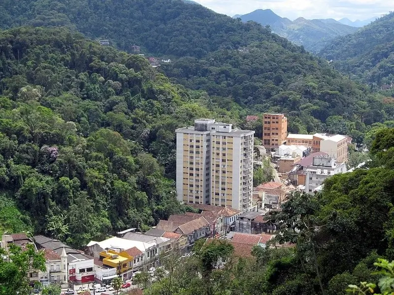 Vista aérea do centro de Petrópolis com prédios entre montanhas cobertas por mata atlântica.