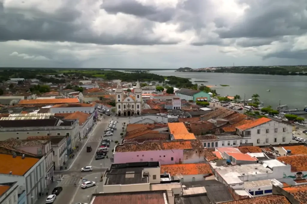 Vista aérea do Centro Histórico de Penedo com igreja, casarios coloniais e Rio São Francisco ao fundo.