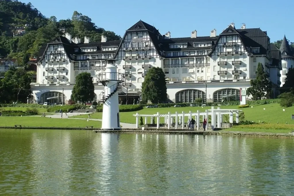 Fachada do Hotel Palácio Quitandinha em Petrópolis refletida no lago em um dia ensolarado.