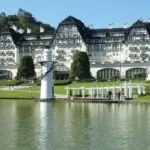 Fachada do Hotel Palácio Quitandinha em Petrópolis refletida no lago em um dia ensolarado.