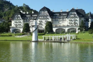 Fachada do Hotel Palácio Quitandinha em Petrópolis refletida no lago em um dia ensolarado.