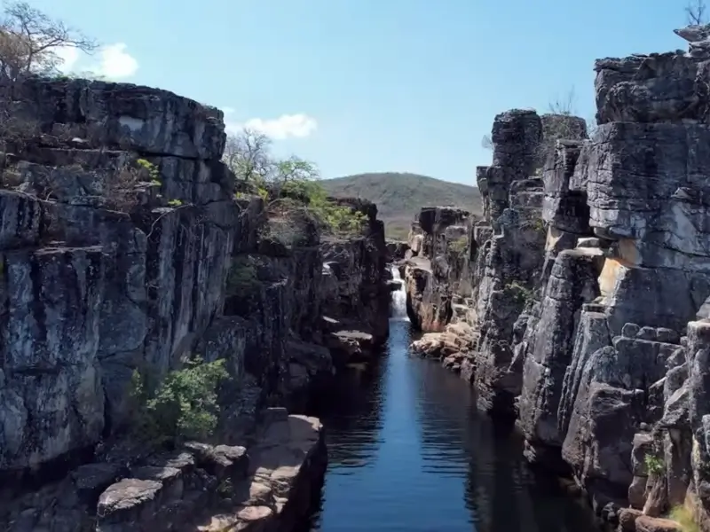 Cânion estreito com paredes rochosas e água escura na Chapada dos Veadeiros em dia ensolarado.