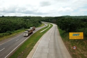 Trecho duplicado da BR-163 com caminhões em circulação, cercado por vegetação, em área estratégica de transporte rodoviário no Mato Grosso.
